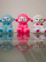 Sheep dolls of different colors placed together showing their reflections on the glass.