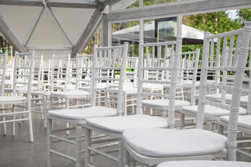 Empty white chairs for guests at a banquet or wedding on an outdoor summer area are in a row