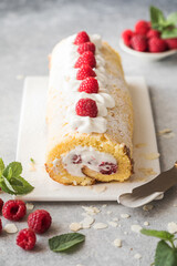Sponge cake roll filling cream and raspberries, on white stone background. Soft focus. Summer food concept