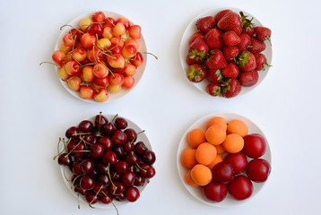Four white plates with different berries on a white background