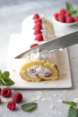 Sponge cake roll filling cream and raspberries, on white stone background. Soft focus. Summer food concept
