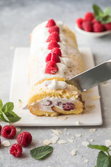 Sponge cake roll filling cream and raspberries, on white stone background. Soft focus. Summer food concept