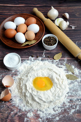 Egg in flour, rolling pin, eggs on a plate, bay leaf, salt and pepper on a dark wooden background