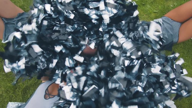 Top view of smiling cheerleader girls in uniform lying with pompoms on green field