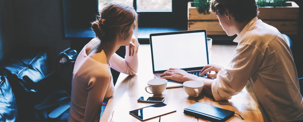 Back view of skilled male and female students downloading media files on laptop computer with blank...