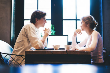 Young caucasian man and woman sitting at cafeteria table with laptop computer with mock up screen for text, millennial female students socialising in coffee shop discussing modern technology