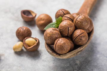 Pile macadamia nuts open kernels and shells in spoon  on stone background.