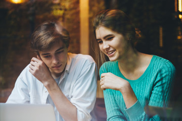 Cheerful male and female friends smiling and spending free time sitting indoors and watching funny videos on laptop,positive hipster guys laughing during browsing information together for coursework