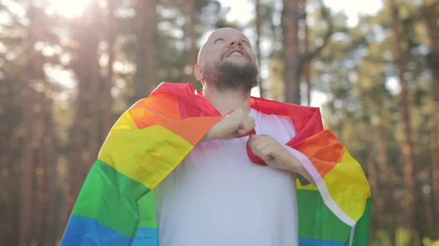 Courageous bold man with beard wrapped in a rainbow gay flag raise up it in sky. LGBTQI, Pride Event, LBGT Pride Month, Gay Pride Symbol