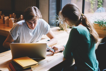 Fototapeta premium Male and female hipster guys prefer messaging with followers in websites using modern gadgets and wireless connection to real conversation while spending leisure time sitting in loft cafeteria