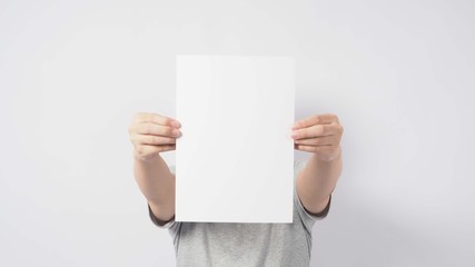 Male's hands is holding the A4 paper and wear gray t shirt and standing on white background.