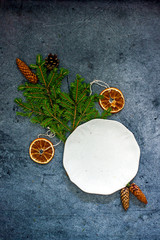Christmas composition with a white plate, fir branches, cones, Christmas decorations on a dark blue background, top view, copy space, flat lay.Christmas background frame,  vertical background