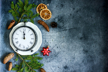 New Year composition with a clock showing the eve new Year. Antique clock with a Roman dial on a dark background decorated with fir branches, cones, dried oranges, Christmas decorations copy space
