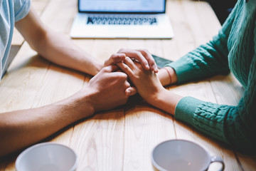 Fototapeta premium Cropped image of man and woman in love steady holding each other hands.Concept of sincere and trust relationship between young male and female sitting at wooden table in comfortable place