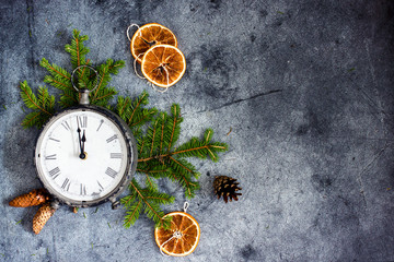 New Year composition with a clock showing the eve new Year. Antique clock with a Roman dial on a dark background decorated with fir branches, cones, dried oranges, Christmas decorations copy space