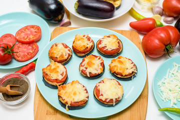 cooking homemade vegan pizza eggplant bites, tomatoes, peppers, mozzarella on a blue plate. eggplant stacked on a light background