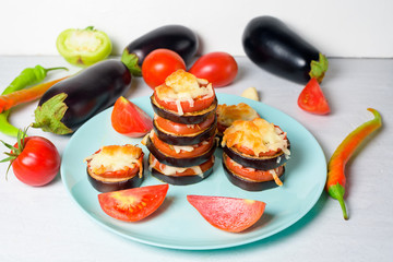 cooking homemade vegan pizza with eggplant on a bite, tomatoes, peppers, mozzarella on a blue plate. eggplant piled up on a light background
