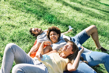Three friends enjoy the sun lying on a grassland without  face mask on a summer day