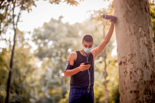 Young Adult Handsome Caucasian Man Resting After Hard Run On Nature. He Wearing A Protective Face Mask.