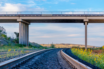 Railway tracks passing under a road bridge against a blue sky
