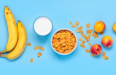 Breakfast cereals, bananas, apricots and a glass of milk on a bright blue background top view, flat lay. Fitness food concept. Breakfast with cornflakes, milk and fruit. Copy space.