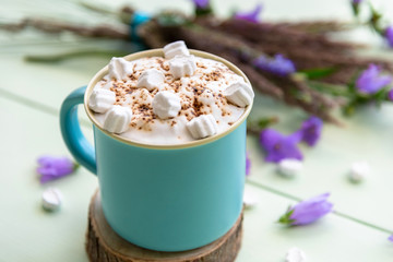 Hot cappuccino with marshmallows and foam in a light blue Cup with flowers.