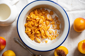 Breakfast cereal in a rustic style. Cornflakes with milk and apricots on a served table top view. Tasty breakfast