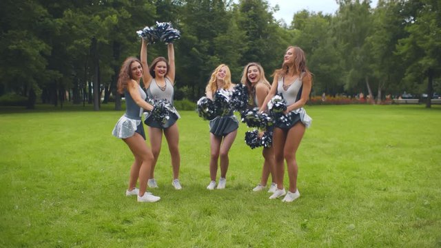 Group of excited cheerleading girls shaking pompons smiling at camera