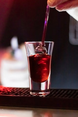 Bartender prepares alcoholic cocktail in night bar. Short drink at bar. Colorful neon lights, dark shadows.