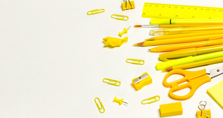 The concept of going back to school. Yellow school supplies, pencils, pens, markers, paper clips, ruler, buttons, scissors on a white background. Space for text
