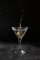 martini with olive splash on dark background