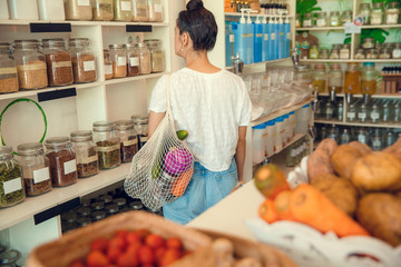 Young woman shopping in zero waste plastic free store with reusable mesh bag. Low waste lifestyle. Sustainable eco lifestyle