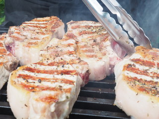 pork cooking pork steaks on the coals. meat on the bone. grill grate.