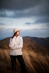 Beautiful woman in a white sweater stands on a mountain top peacefully gazing at morning clouds and the pastel colours of a tranquil sunrise - 371493379