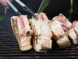 a cook in a black apron roasts steaks meat on the bone. grilled pork on the bone. tongs for grilling.