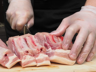 a chef in gloves and a black apron cuts a pork loin into steaks. the cooking of the steaks. meat. pork.