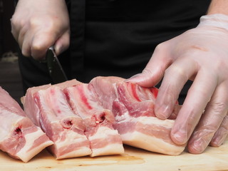 a chef in gloves and a black apron cuts a pork loin into steaks. the cooking of the steaks. meat. pork.
