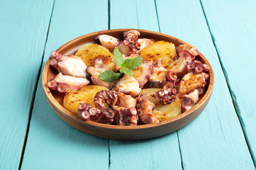 Cooked octopus dish served with sliced boiled potatoes, smoked paprika and olive oil. on blue wooden background