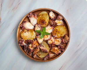 Cooked octopus dish served with sliced boiled potatoes, smoked paprika and olive oil. On marble background