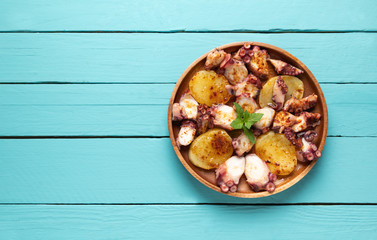 Cooked octopus dish served with sliced boiled potatoes, smoked paprika and olive oil. on blue wooden background, top view