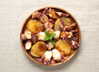 Cooked octopus dish served with sliced boiled potatoes, smoked paprika and olive oil. top view