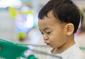 An Adorable toddler Asian boy (1-year-old) sitting and play inside the trolley with blurry supermarket background.