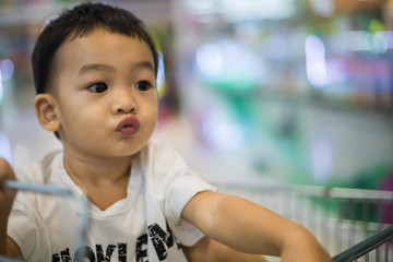 An Adorable toddler Asian boy (1-year-old) sitting and play inside the trolley with blurry supermarket background.