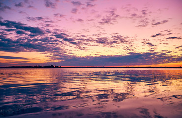 Raspberry sunset on the shore. Mirror reflection of a cloudy sky in the water. Calm on the river.