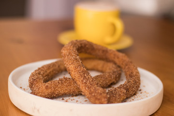 Churros azucarados con taza de chocolate caliente amarilla al fondo. 