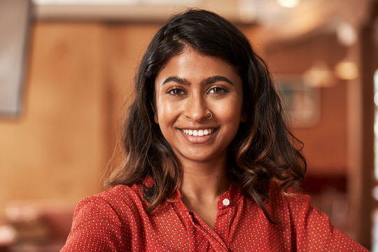 Portrait of young ethnic woman wearing orange blouse sitting at bar in kitchen of downtown loft 
