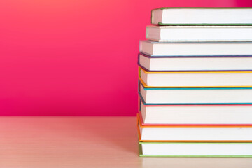 Stack of colorful books, bright colorful pink background, free copy space. Books on table, no labels, blank spine. Back to school. Education background