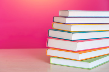 Stack of colorful books, bright colorful pink background, free copy space. Books on table, no labels, blank spine. Back to school. Education background