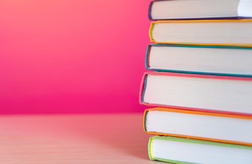 Stack of colorful books, bright colorful pink background, free copy space. Books on table, no labels, blank spine. Back to school. Education background