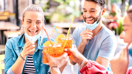 Friends drinking at cocktail bar with open face masks - New normal lifestyle concept with happy people having fun together toasting drinks at restaurant - Bright vivid filter with focus on left woman
